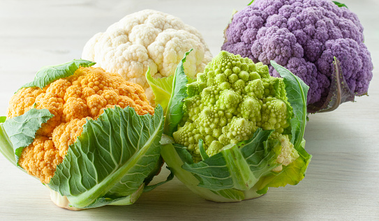 different types of cauliflowers with green leaves and colorful flower heads on a wooden table