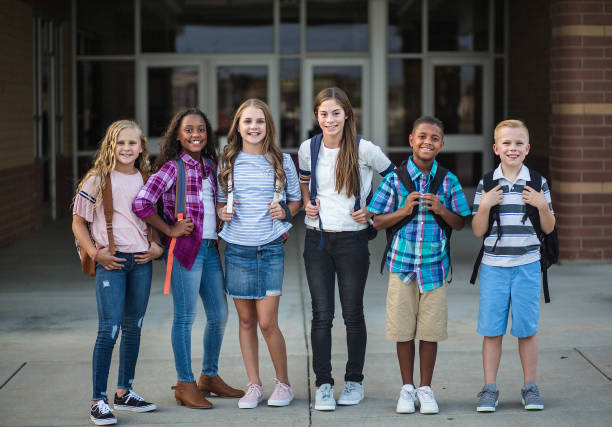 Group portrait of pre-adolescent school kids smiling in front of the school building Large Group portrait of pre-adolescent school kids smiling in front of the school building. Back to school photo of a diverse group of children wearing backpacks and ready to go to school elementary school building photos stock pictures, royalty-free photos & images