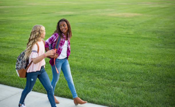 Two diverse school kids walking home together after school Two diverse school kids walking home together after school and talking together. Back to school photo of diverse girls wearing backpacks in the school yard only girls stock pictures, royalty-free photos & images