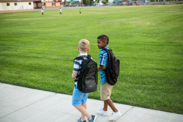due diversi scolari che camminano e parlano insieme sulla strada per la scuola - untucked foto e immagini stock