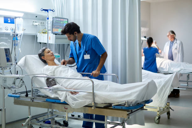 eine männliche krankenschwester hört mit einem stethoskop das herz eines patienten. - hospital patient bed doctor stock-fotos und bilder