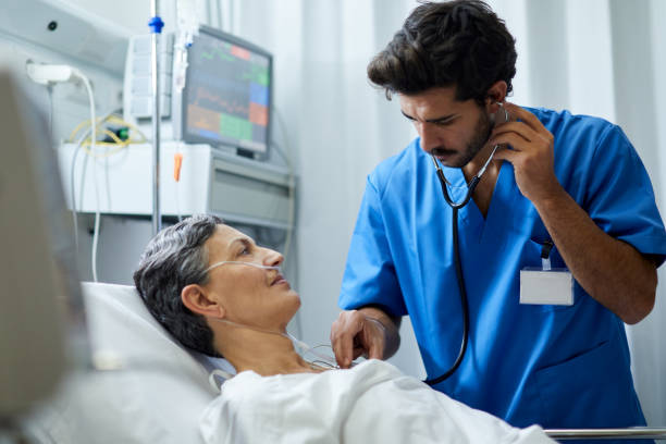 um enfermeiro está ouvindo com um estetoscópio o peito de um paciente. - hospital patient bed doctor - fotografias e filmes do acervo