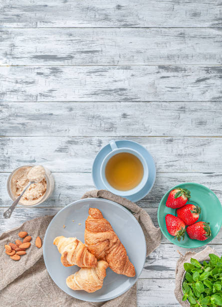 istock Breakfast. With a cup of tea, fresh croissants, fragrant strawberries and coconut paste. Composition on a gray wooden background. Place for text. Flat lay. Vertical image. 1217096140