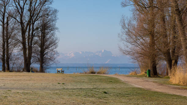 Starnberg, Bavaria / Germany - Mar 31 2020: Path leading along Lake Starnberg (Starnberger See). With Wetterstein Mountains (incl. Zugspitze) in the far distance.