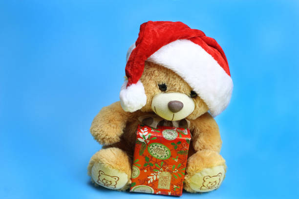 istock Teddy bear in Santa Claus hat holding a Christmas gift. Blue background 1217098792