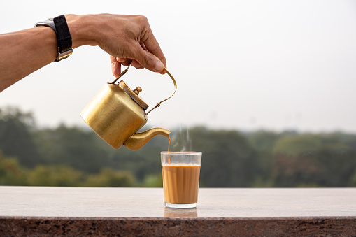 Verter a mano el té masala de una tetera en un vaso. photo