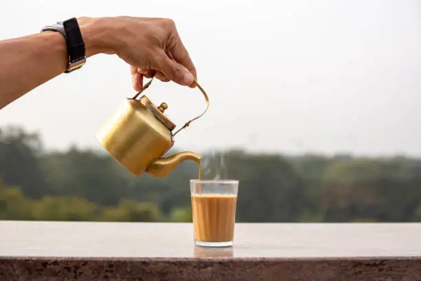 Photo of Hand pouring masala tea from a teapot into a glass.