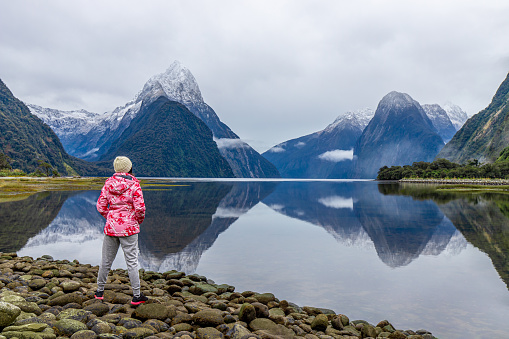 Young Asian traveler girl from back standing at Milford Sound; Fiordland National Park, South Island, New Zealand NZ