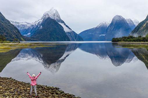 Young Asian traveler celebrating success at Milford Sound, Fiordland National Park, South Island, New Zealand NZ