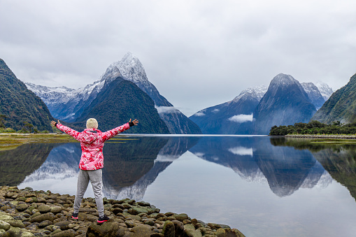 Young Asian traveler celebrating success at Milford Sound, Fiordland National Park, South Island, New Zealand NZ
