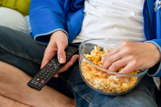 Coronavirus stay at home quarantine self isolation entertainment concept. Man sitting with the bowl of popcorn and holding a tv remote. Unealthy lifestyle. Coronavirus stay at home quarantine self isolation entertainment concept. Man sitting with the bowl of popcorn and holding a tv remote. Unealthy lifestyle. popcorn snack bowl isolated stock pictures, royalty-free photos & images
