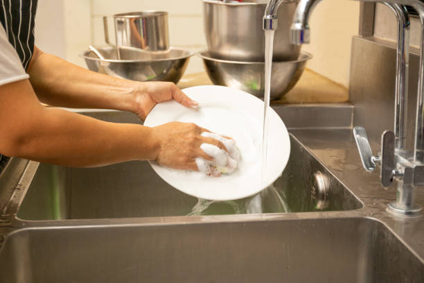 istock Hands washing dirty dishes with running water in kitchen sink. 1217106934