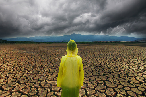 Young man wear a raincoat standing on midle dry lake with storm cloud metaphor climate change and extreme weather on summer