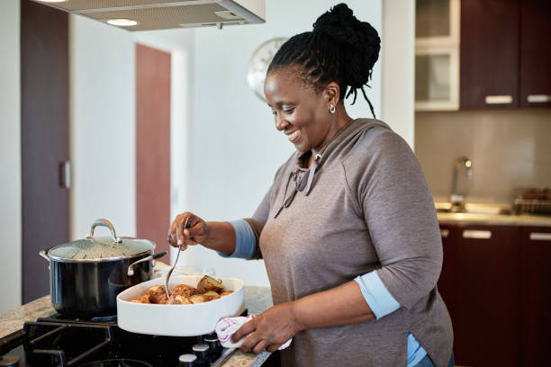 istock Smiling Mature African Woman Roasting Potatoes in Kitchen 1217111705