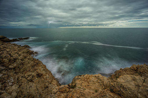 Seascape on the coast of Saint-Jean-Cap-Ferrat in French Riviera. Sea surf shot with long exposure. There are lightnings on the horizon.