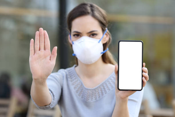 istock Girl with mask gesturing stop showing blank phone screen 1217114501
