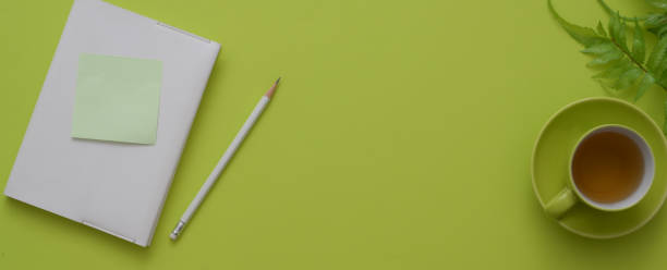 Top view of workspace with diary notebook, tea cup, decoration and copy space on green table