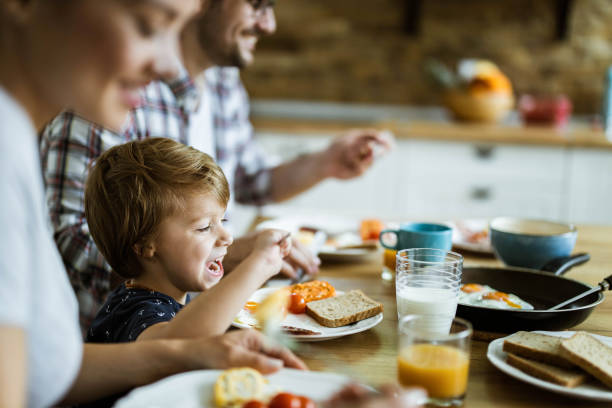 menino feliz tomando café da manhã com seus pais na mesa de jantar. - little boys breakfast caucasian child - fotografias e filmes do acervo