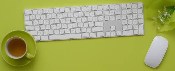 Top view of workspace with computer devices, tea cup and decoration on green table