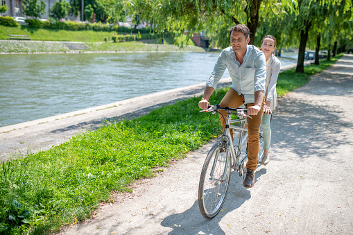 Smiling mature couple riding tandem bicycle in park.