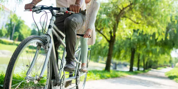 Low section of mature couple riding tandem bicycle in park.