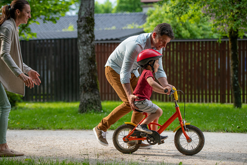 Mature father teaching his son to ride bicycle in park.