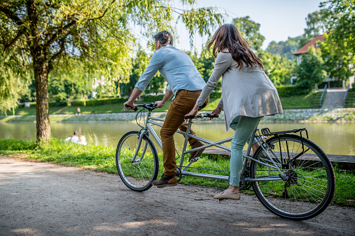 Mature couple riding tandem bicycle in park.