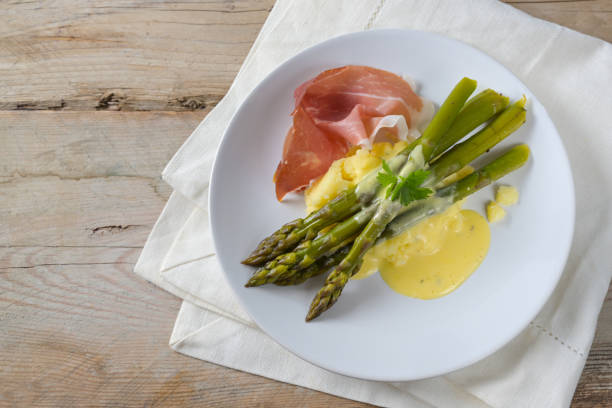 istock Green asparagus with mashed potatoes, ham and a light hollandaise sauce on a white plate on rustic wooden planks, copy space, high angle view from above 1217119415