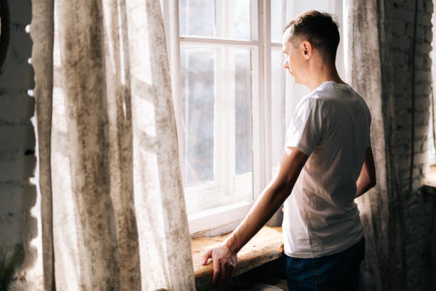 istock Thoughtful young man stands by the window on sunny day. 1217124879