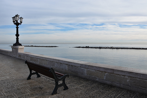 Tranquil morning with calm sea and mild sunlight, empty bench, no people on sea promenade of Bari, Italy