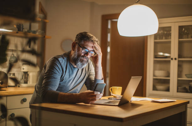 Working during isolation period Mature men at home during pandemic isolation reading something on laptop depression behavior businessman economic depression stock pictures, royalty-free photos & images