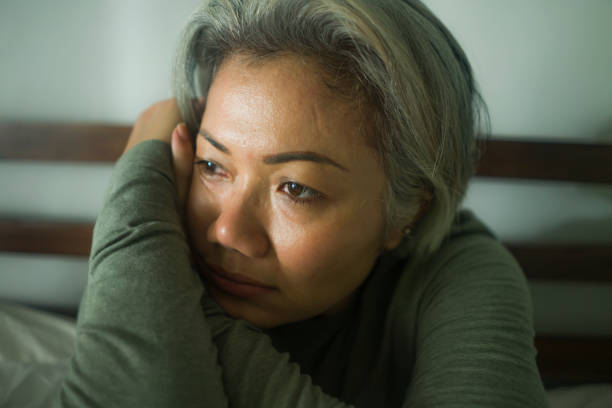 mature lady crisis - attractive middle aged woman with grey hair sad and depressed in bed feeling scared and lonely thinking worried about covid-19 virus pandemic during home lockdown stock photo