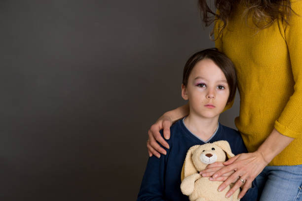 istock Sad boy with bruised eye, hugging mom and teddy bear at home 1217130012