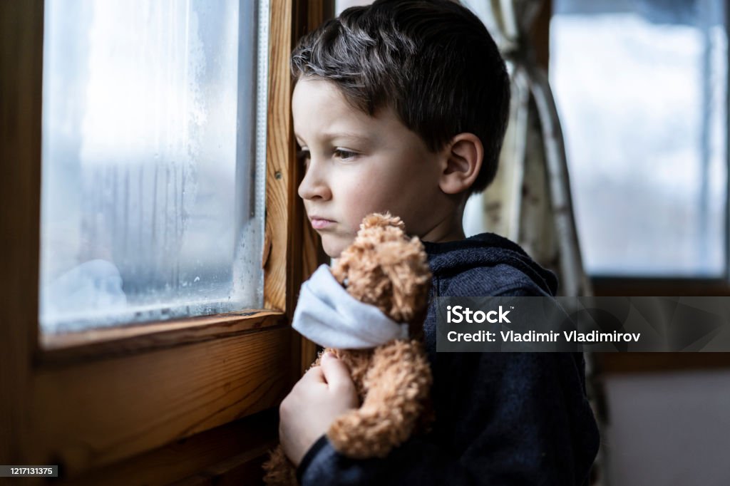 Kleiner trauriger Junge, der während der Coronavirus-Isolation durch das Fenster schaut. - Lizenzfrei Kind Stock-Foto