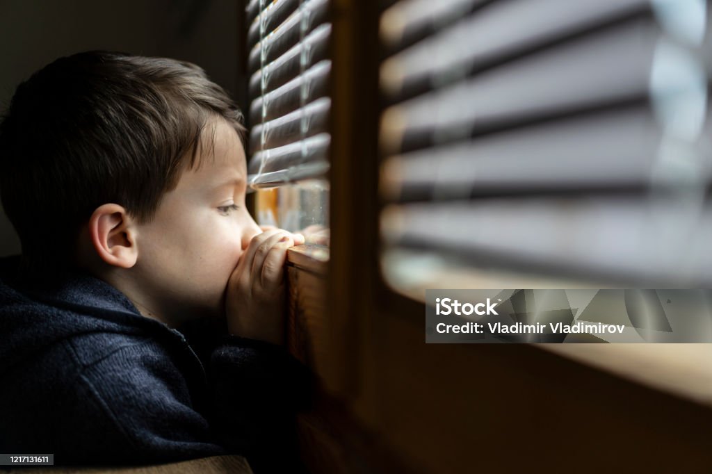 Small sad boy looking through the window during Coronavirus isolation. Small sad boy looking through the window. Concept for social distancing during coronavirus pandemic Child Stock Photo