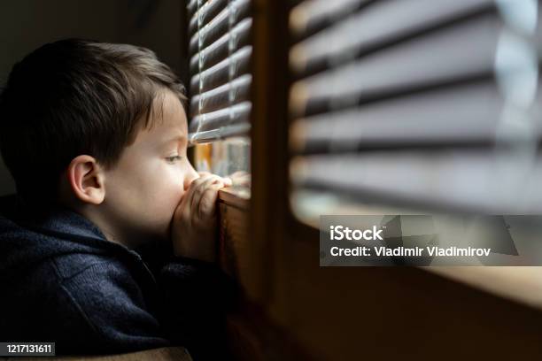 Small Sad Boy Looking Through The Window During Coronavirus Isolation Stock Photo - Download Image Now