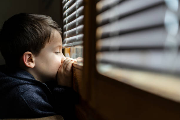 mały smutny chłopiec patrząc przez okno podczas izolacji coronavirus. - loneliness solitude sadness depression zdjęcia i obrazy z banku zdjęć