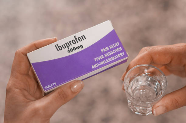 Woman hold a box of 400mg ibuprofen tablets in her hand and a glass of water Woman hold a box of 400mg ibuprofen tablets in her hand and a glass of water cristian stock pictures, royalty-free photos & images