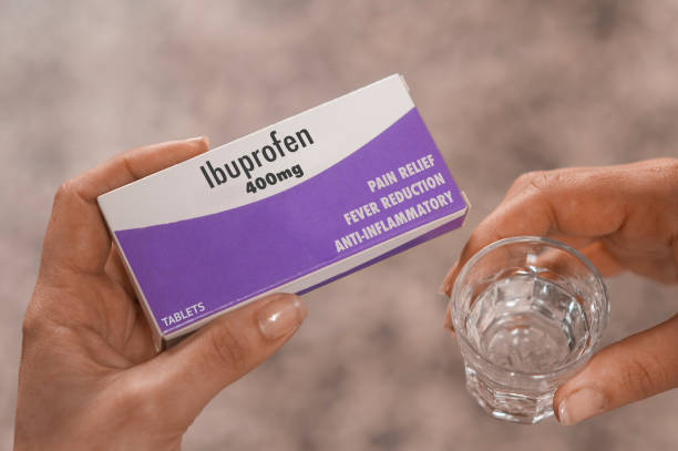 mulher segura uma caixa de comprimidos de ibuprofeno de 400mg na mão e um copo de água - cristian - fotografias e filmes do acervo