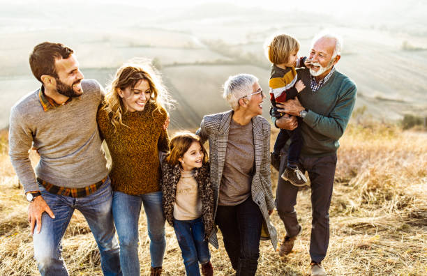 glückliche mehrgenerationenfamilie im gespräch, während sie auf dem feld spazieren geht. - familie mit mehreren generationen stock-fotos und bilder