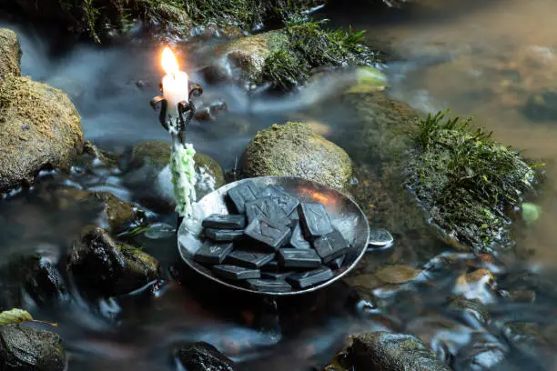 Photo of Norse Runes in a forged bowl with candle. In the evening  on the river