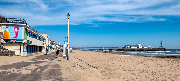 Bournemouth, UK - April 5, 2020: People walking on the Bournemouth Promenade and Pier on a sunny day.