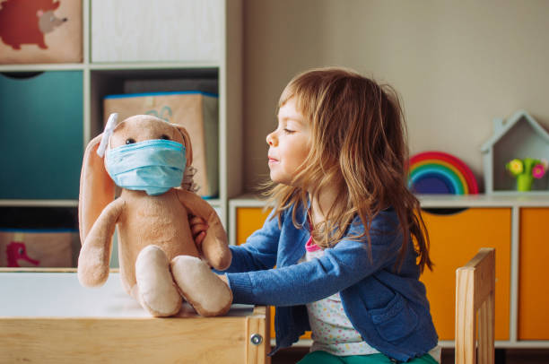 Little girl playing with rabbit soft toy in the medicine mask Little girl playing with rabbit soft toy in the medicine mask sitting at the table in the kids room. doll photos stock pictures, royalty-free photos & images