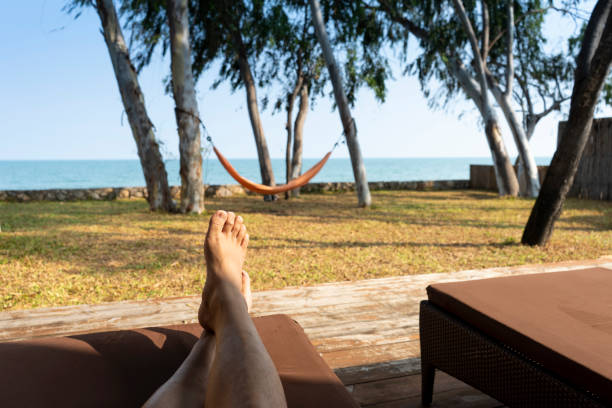 istock Young man sleep rest relaxing under tree shade on beach on sunny summer day with hammock and sea in front of view. Vacation holidays. Man feet closeup on sunbed enjoying sun on weekend. 1217140081