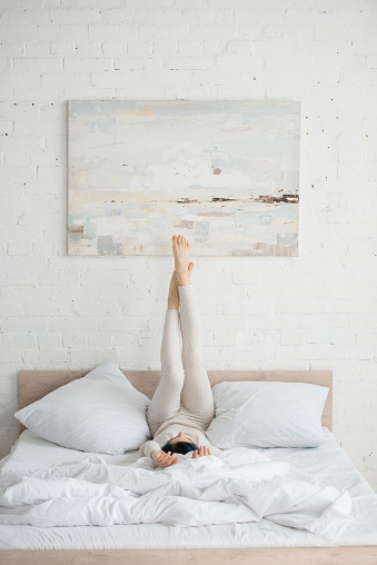 Woman with colorful hair and raised legs lying on bed in bedroom
