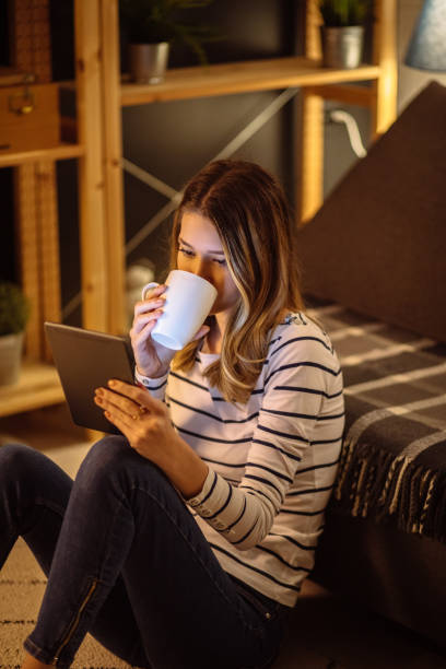 istock Young woman using digital tablet and drinking tea at night in her living room 1217142271