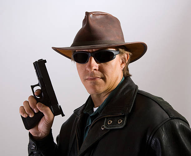 Bounty Hunter A man wearing dark sunglasses in a leather jacket and hat holding a handgun. bounty hunter stock pictures, royalty-free photos & images