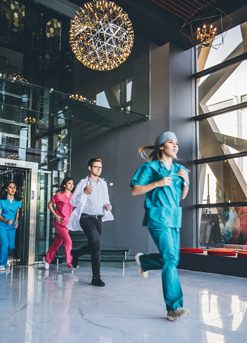 Blurred motion of team of doctors, nurses and medical professionals running down a modern hospital corridor in an emergency calling