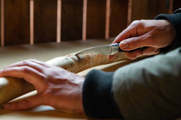 検疫中に木製の歩行棒を屋内で作る人のプロセス。ナイフを使ってテーブルの上に木の棒を彫る - cutting wood holding supporting ストックフォトと画像