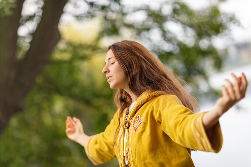 A woman meditating in a forest environment with her arms outstretched.
